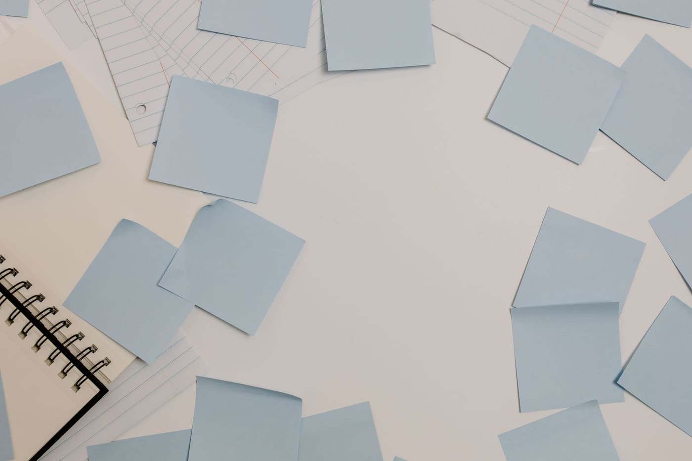 A desk with blue sticky notes, a spiral notepad, and lined papers seen from above