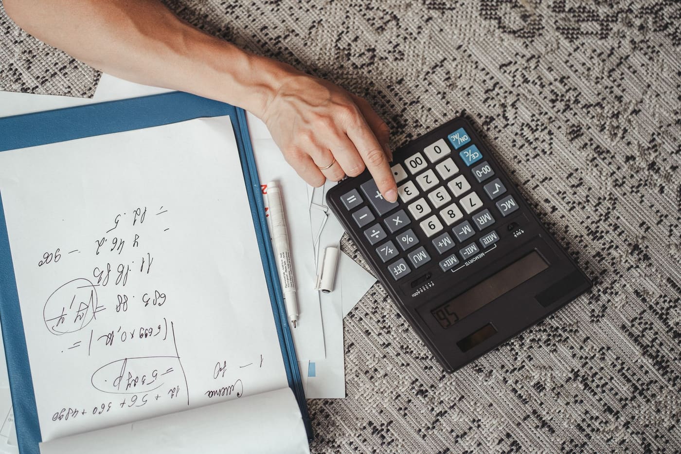 A hand using a large calculator next to handwritten notes on a desk