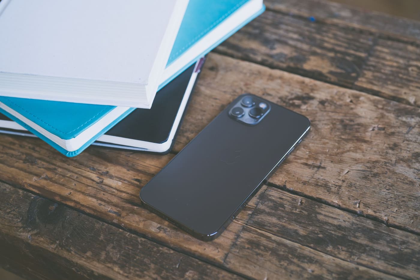 A smartphone lying face down on a wooden table beside a stack of notebooks