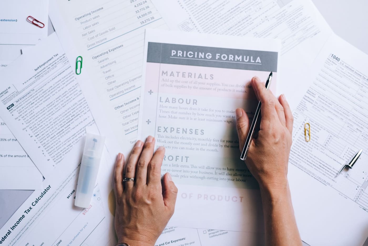 Hands arranging business papers, one headed as a pricing formula, on a desk
