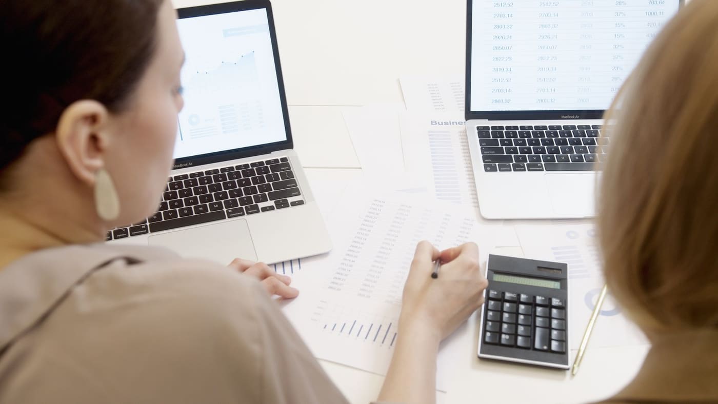 Two people at a table reviewing figures on laptops with a calculator