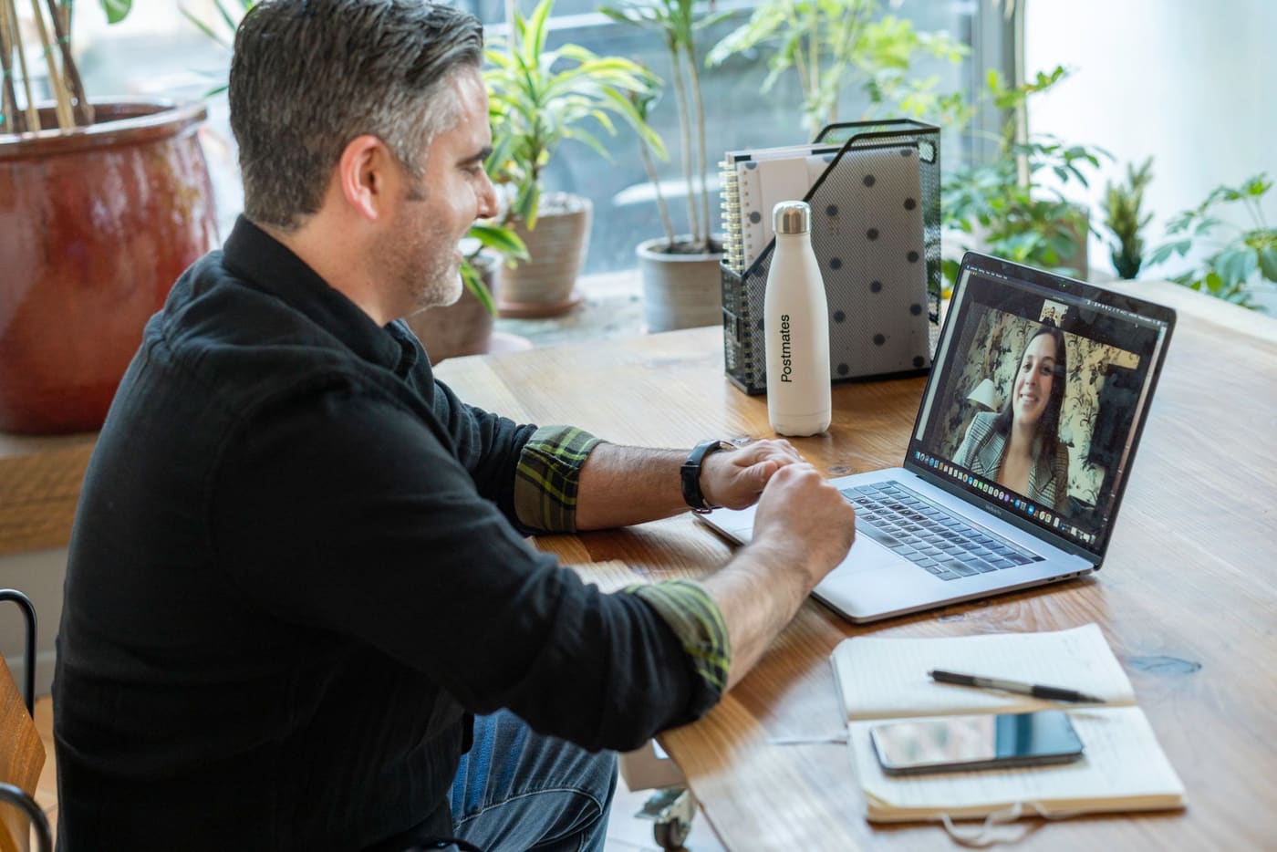 A man taking a video call on a laptop at a home desk with plants nearby