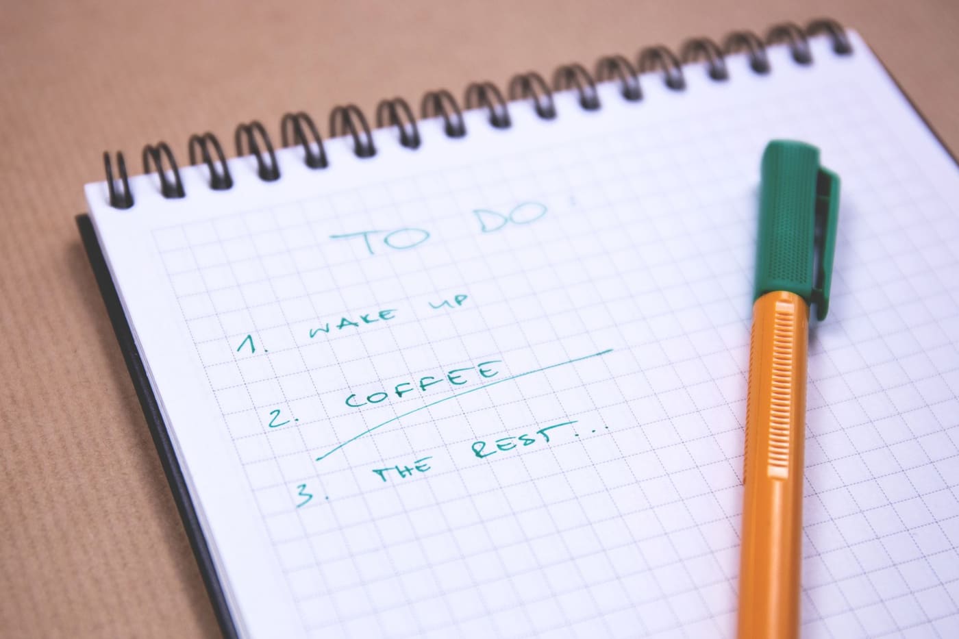 A spiral notebook with a short handwritten to-do list and a pen on graph paper