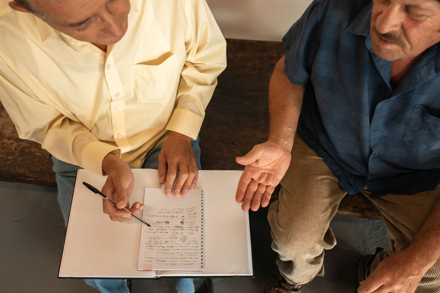 Overhead view of two men in discussion with one writing notes in a notebook
