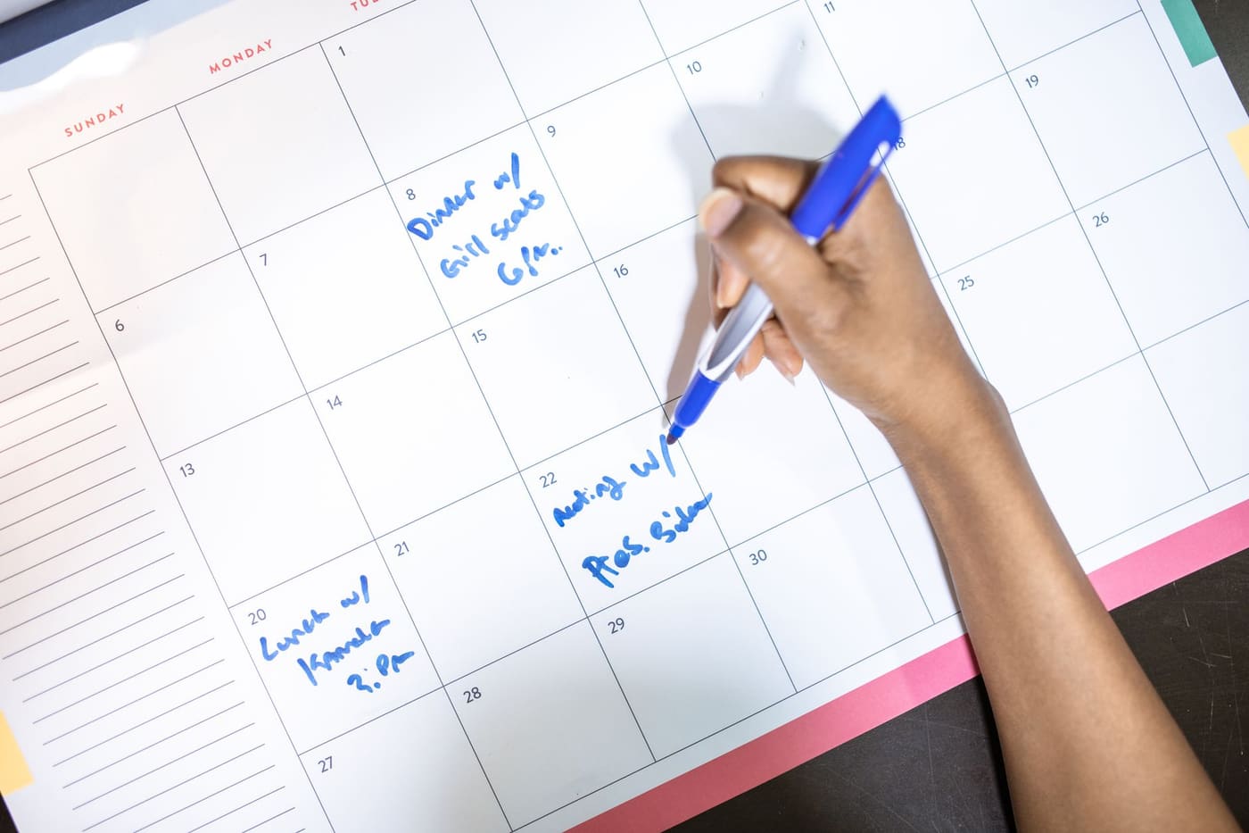 A person writing appointments on a monthly wall calendar with a blue pen